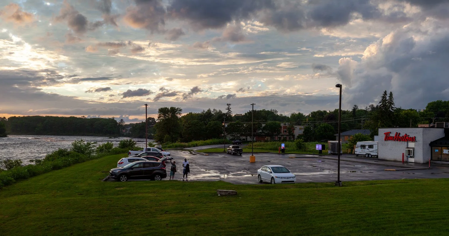 Tim Hortons outlet near a river with parked cars and a sunset sky.