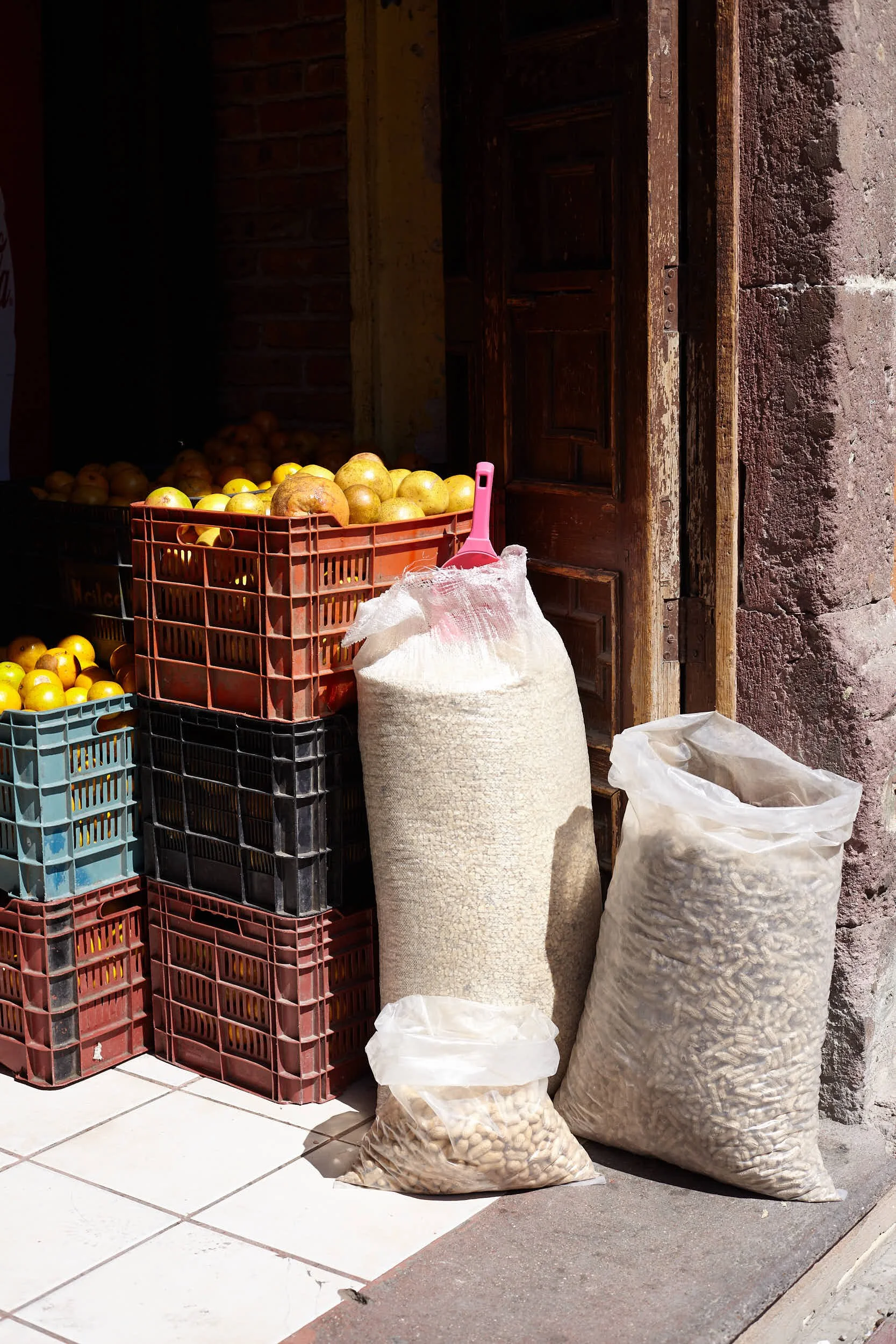 Baskets of yellow apples stacked outside a store, with large bags of rice and beans on the ground beside them.