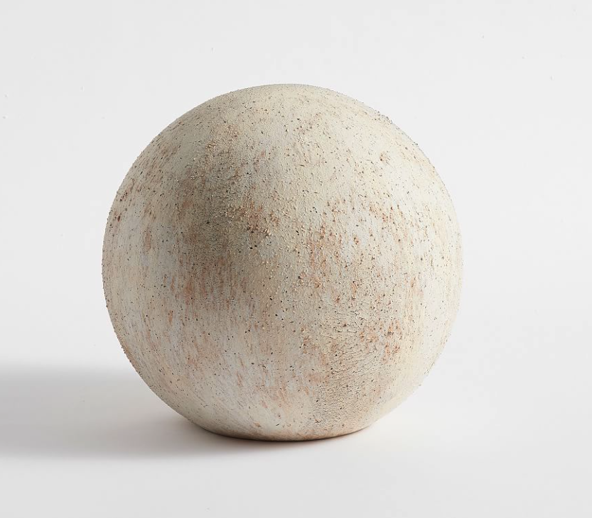 A large, round, textured beige ceramic or plaster sphere with a matte finish, set against a plain white background representing an individual.