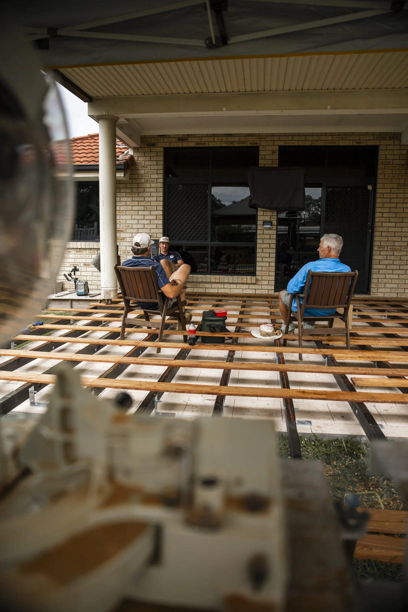 Three men sitting on chairs in front of a house, with a partially built deck.