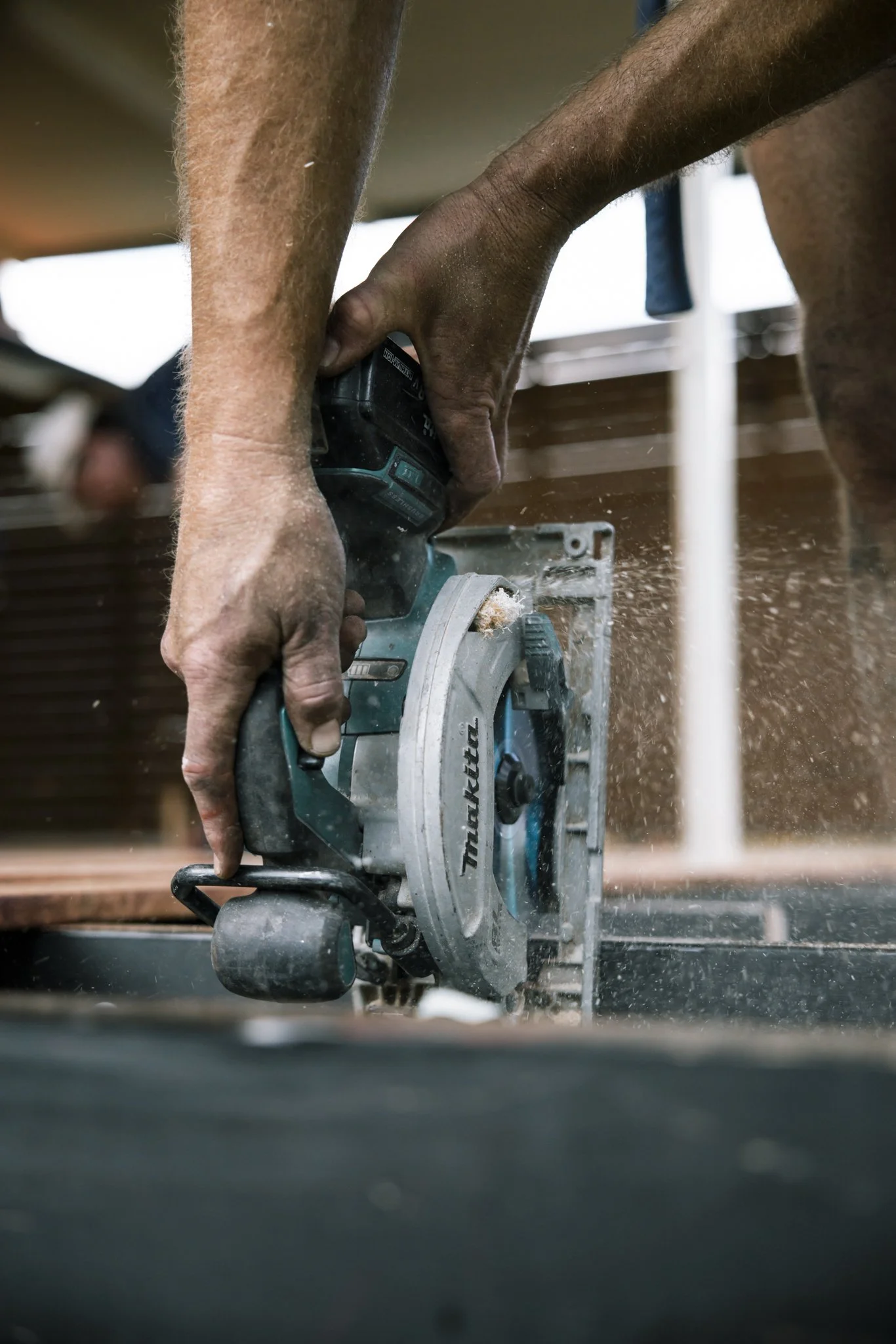 A person using a Makita circular saw to cut wood, with sawdust flying in the air.