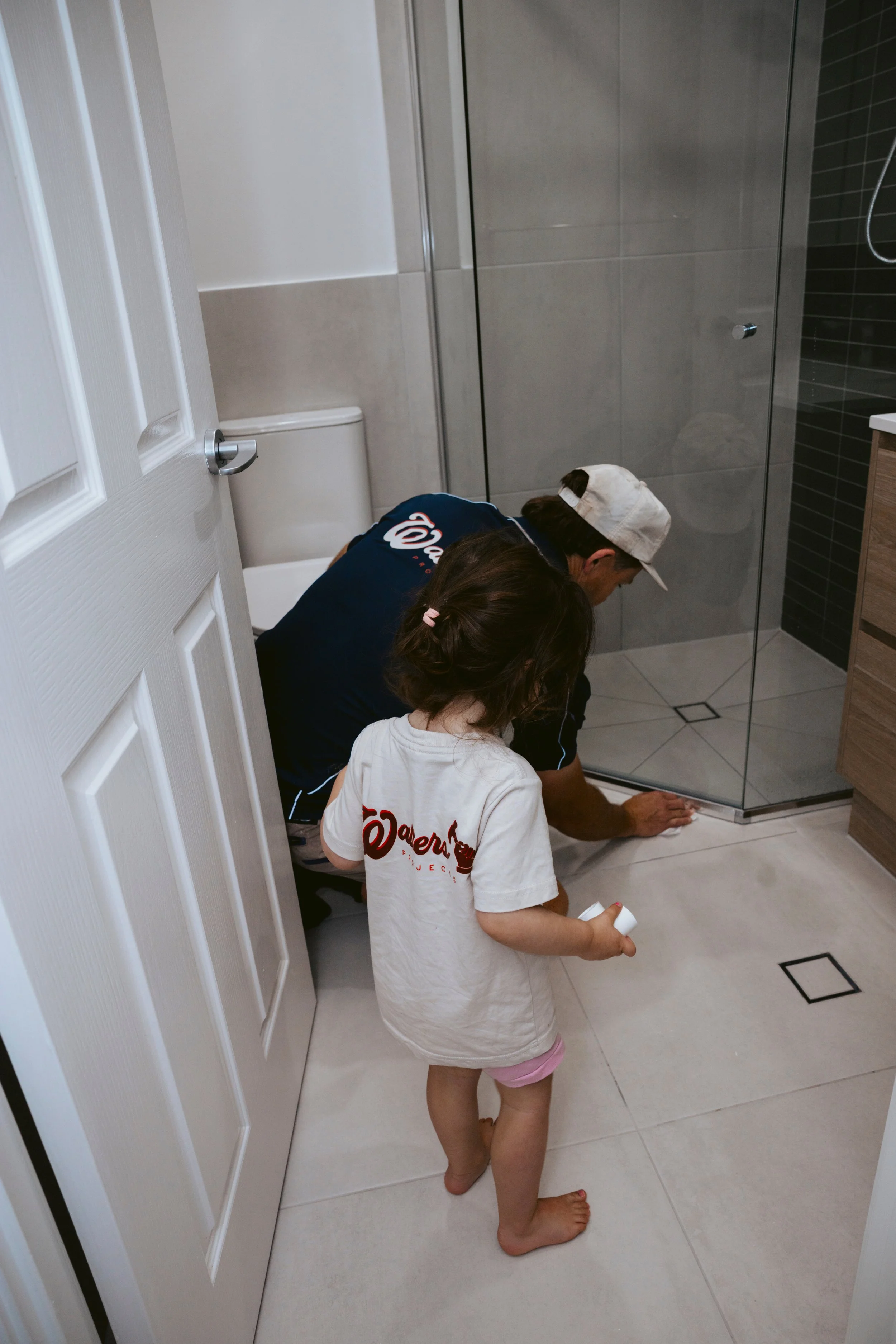 A man and a young girl cleaning the bathroom floor near a glass shower door.