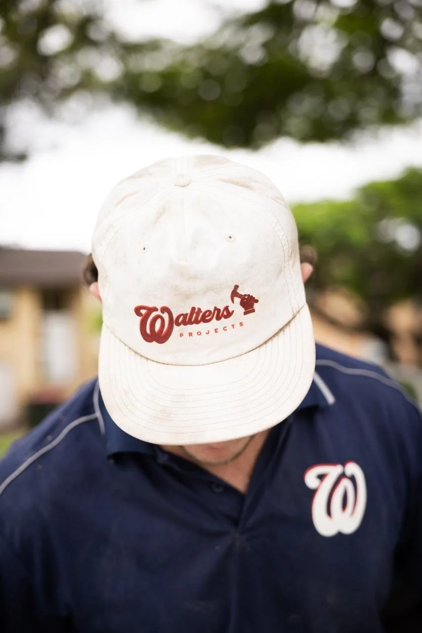 A person wearing a white baseball cap with the Washington Nationals logo and the words 'Walters Projects' embroidered in red, along with a red hammer icon. The person is outdoors, looking down, with a dark blue shirt that also has the Nationals logo 