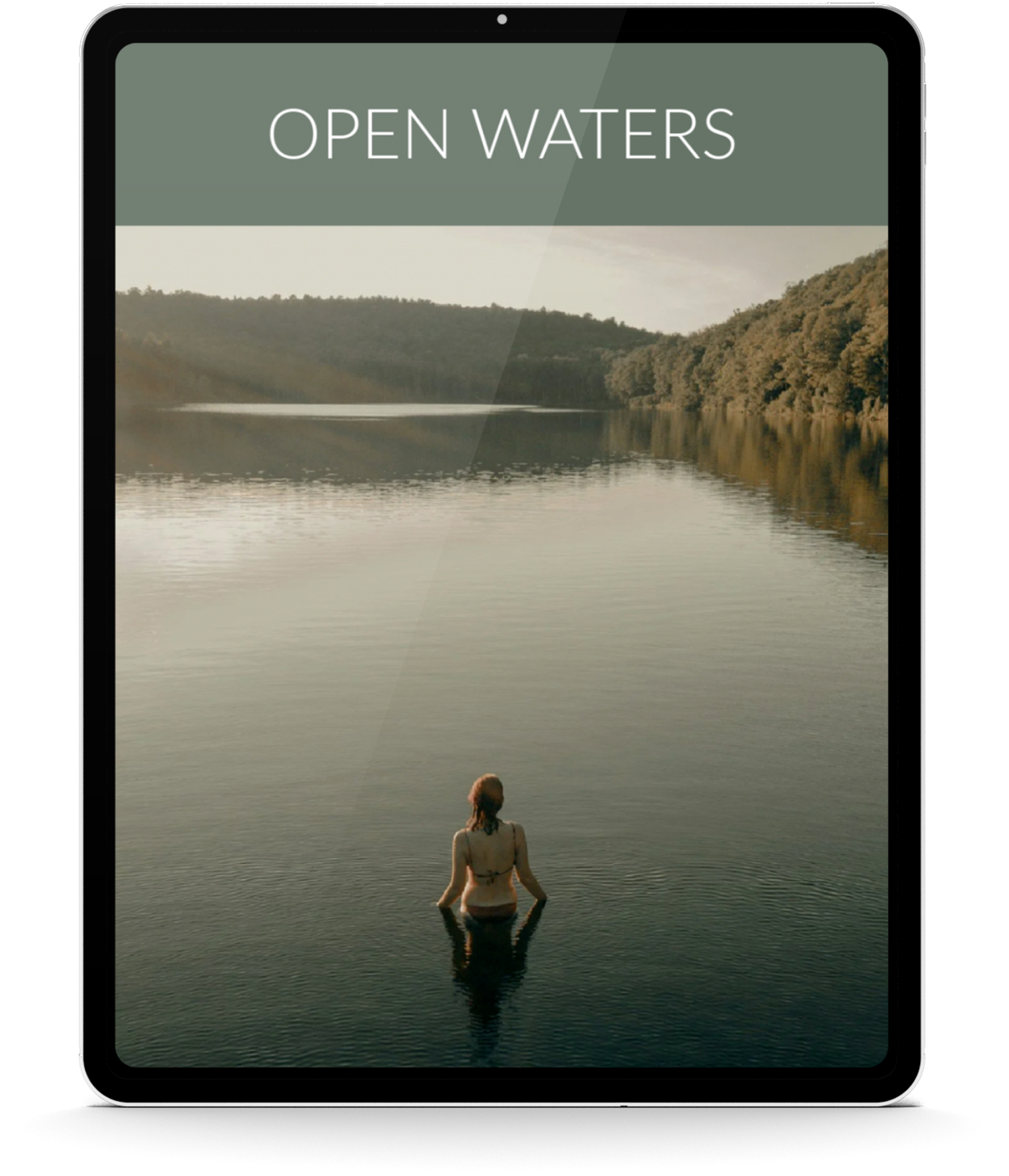 A woman in a swimsuit sitting in water at what appears to be a lake or river, with trees and hills in the background during sunset or sunrise.