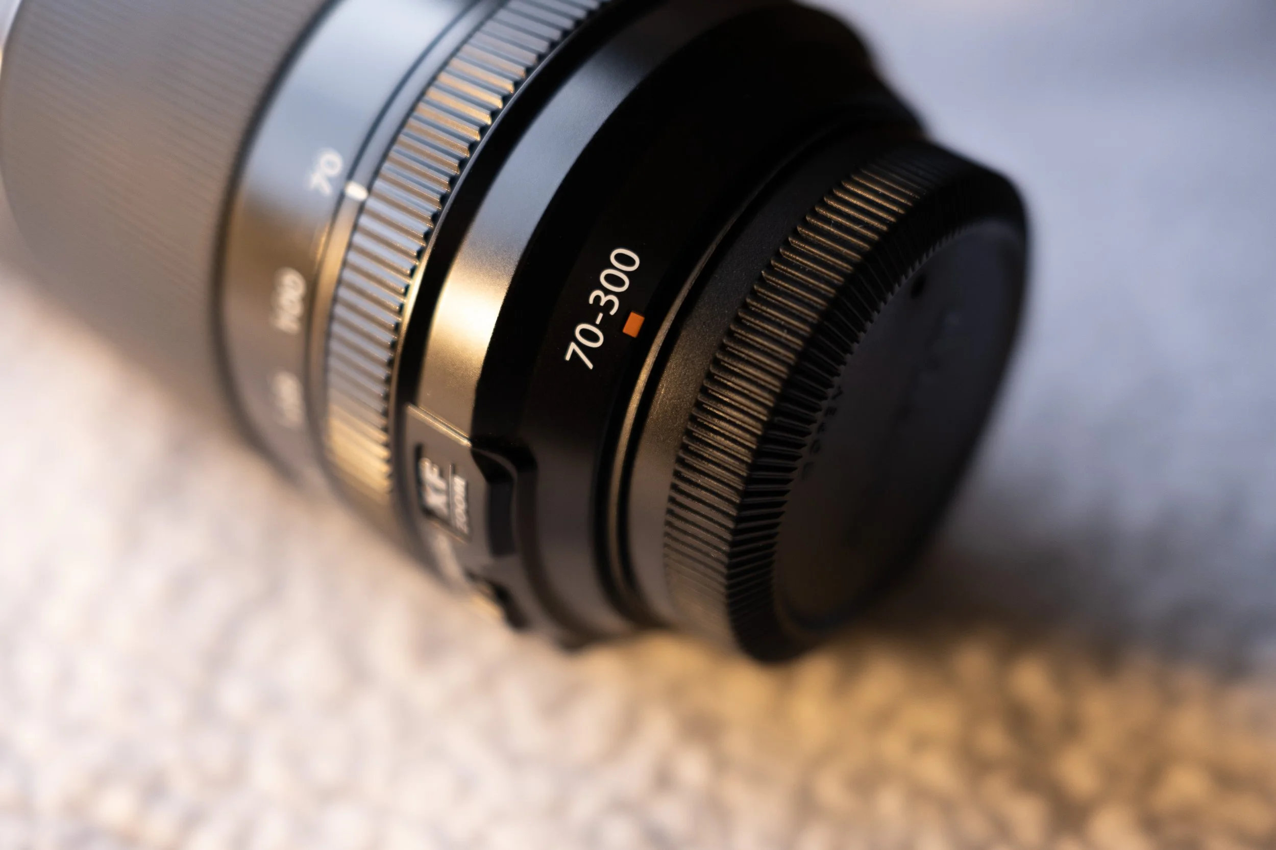 Close-up of a Fujifilm telephoto camera lens with focal length 70-300mm, lying on a textured surface.