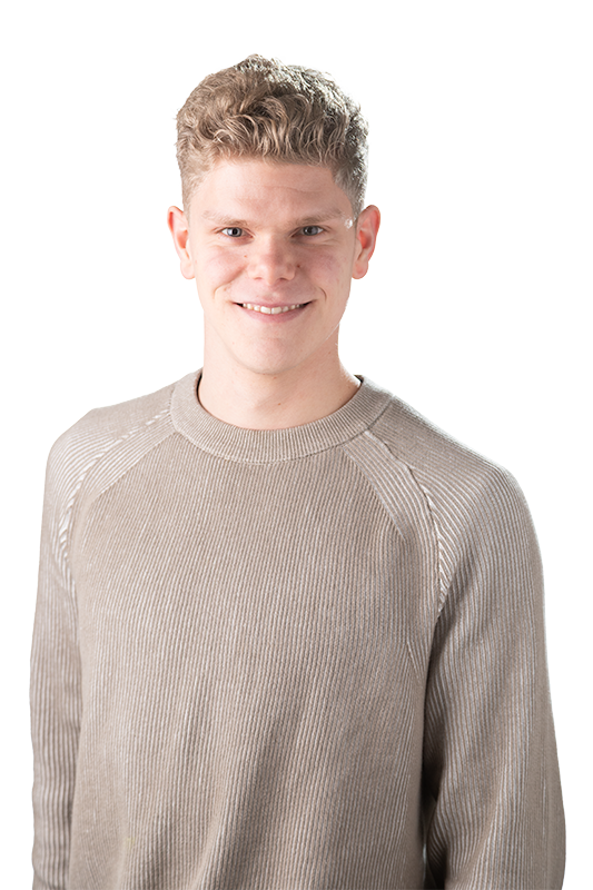 Een jonge man met kort, gekruld blond haar en een lichte huid, dragend een lichtbruin, gewafeld sweater, lachend naar de camera.