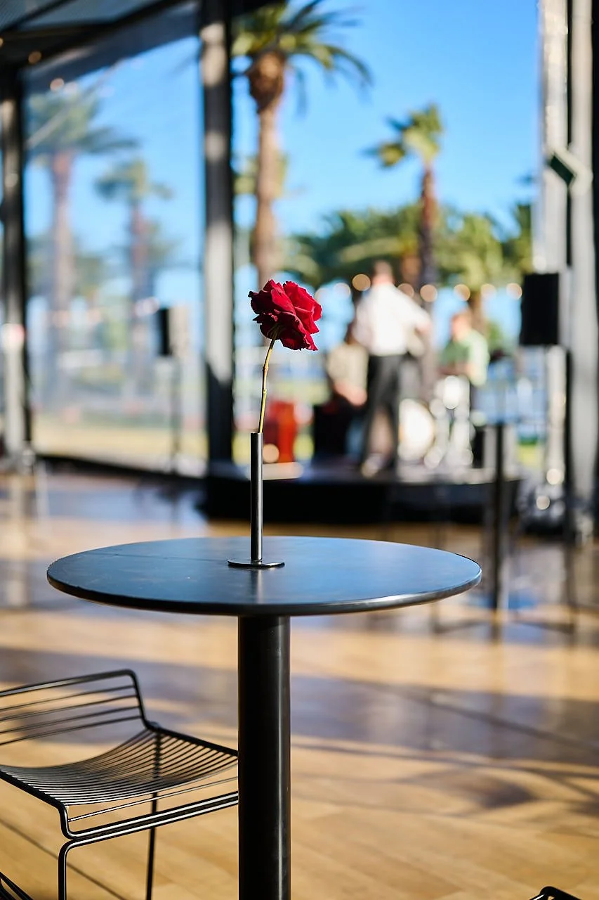Minimal single-stem bud vase featuring a deep red rose on a sleek black cocktail table, styled for a modern moody event aesthetic. Designed and created by Penny Dormer of Wild Heart Flowers – Perth Event Florist.