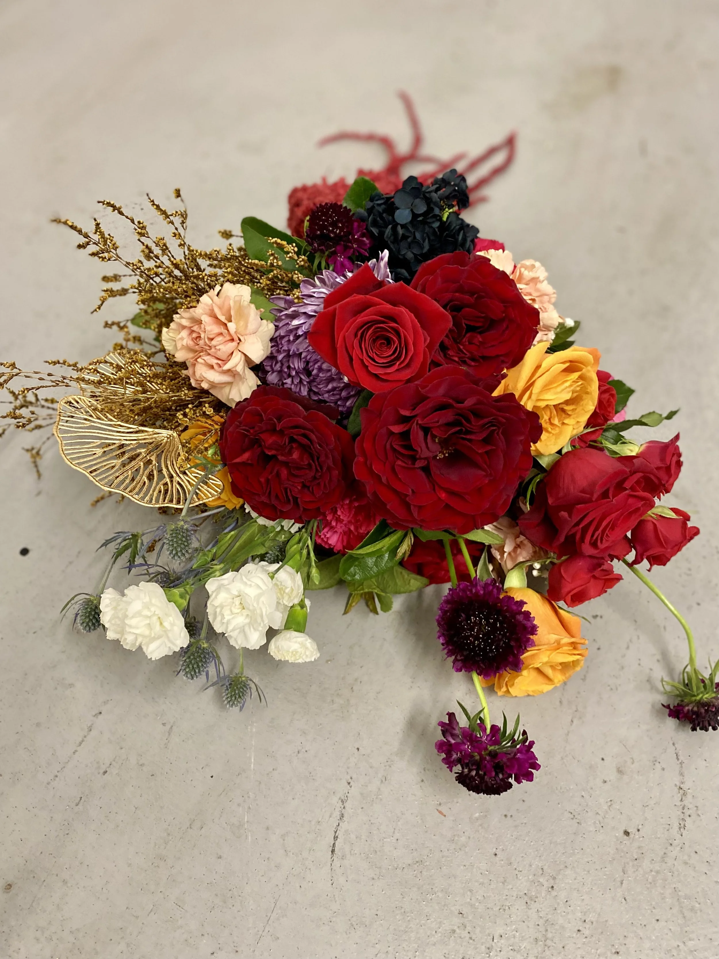 Overhead view of vibrant bridal bouquet with red and yellow roses, black hydrangea, lilac disbuds, pale peach carnations, white lisianthus, and gold ginko. Romantic and bold wedding flowers by Penny Dormer, floral designer in Perth.