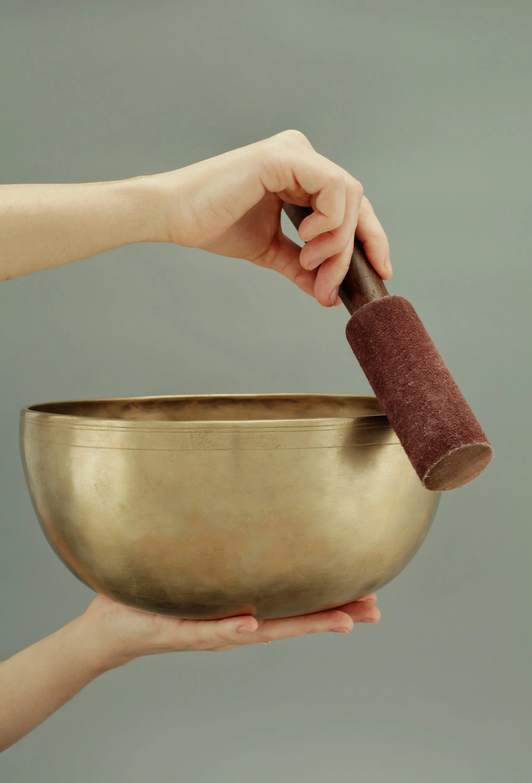 Singing bowl held in one hand, the other hand circling the rim with a mallet.
