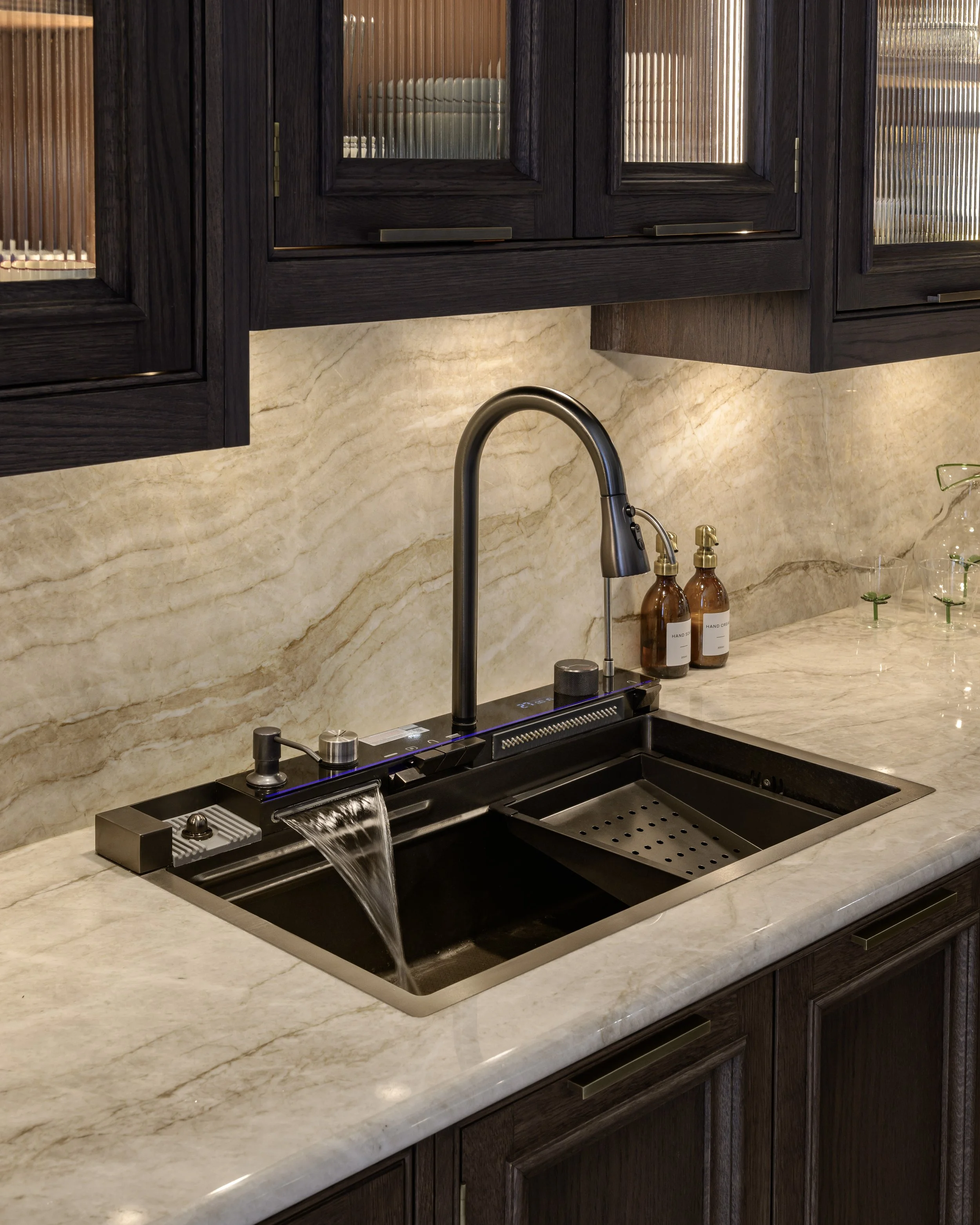 A person pouring a red beverage from an espresso machine into a glass on a wooden cutting board in a modern kitchen.