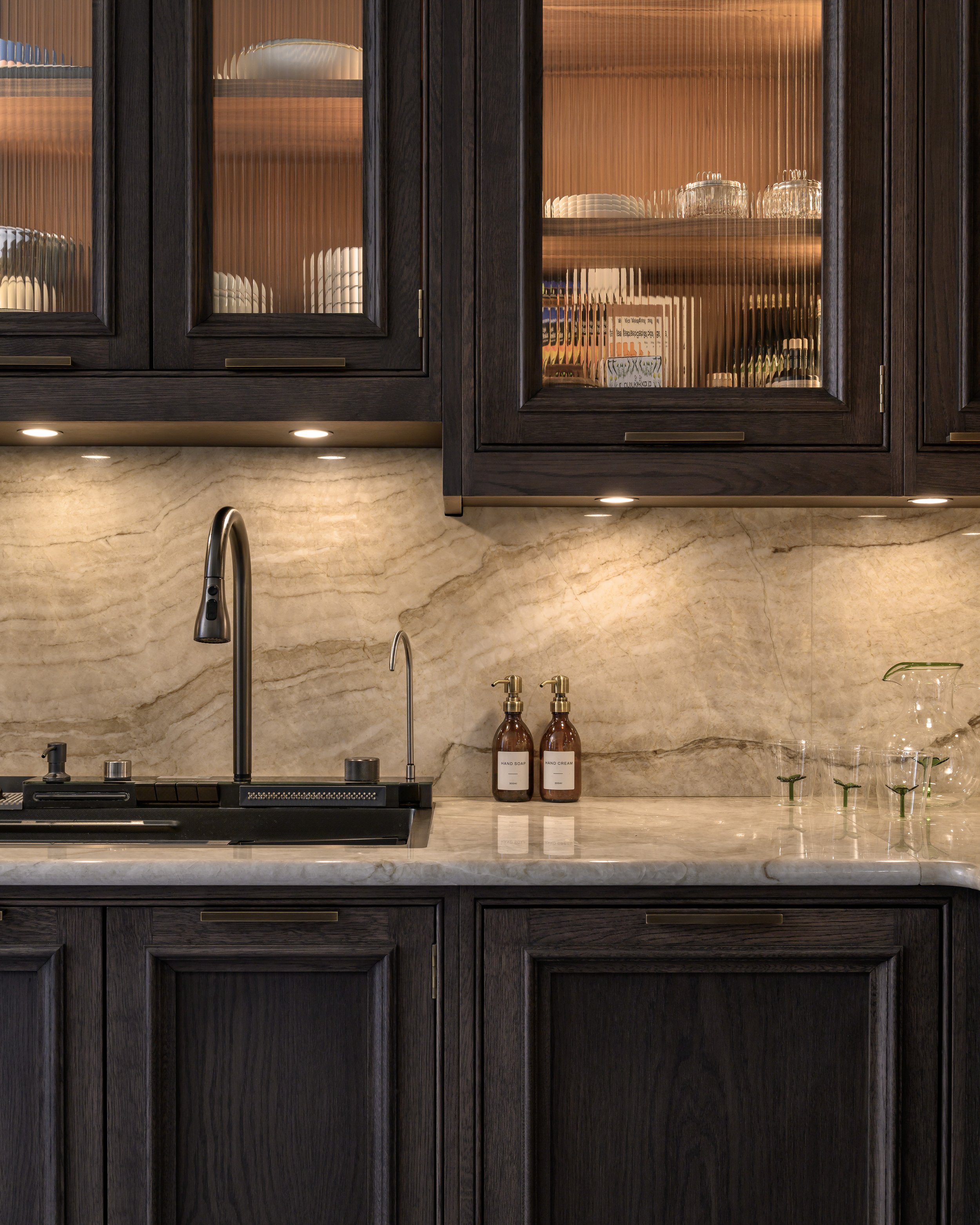 Close-up of a modern kitchen island with a wooden base, a marble countertop, and a brown leather chair part visible in the foreground.