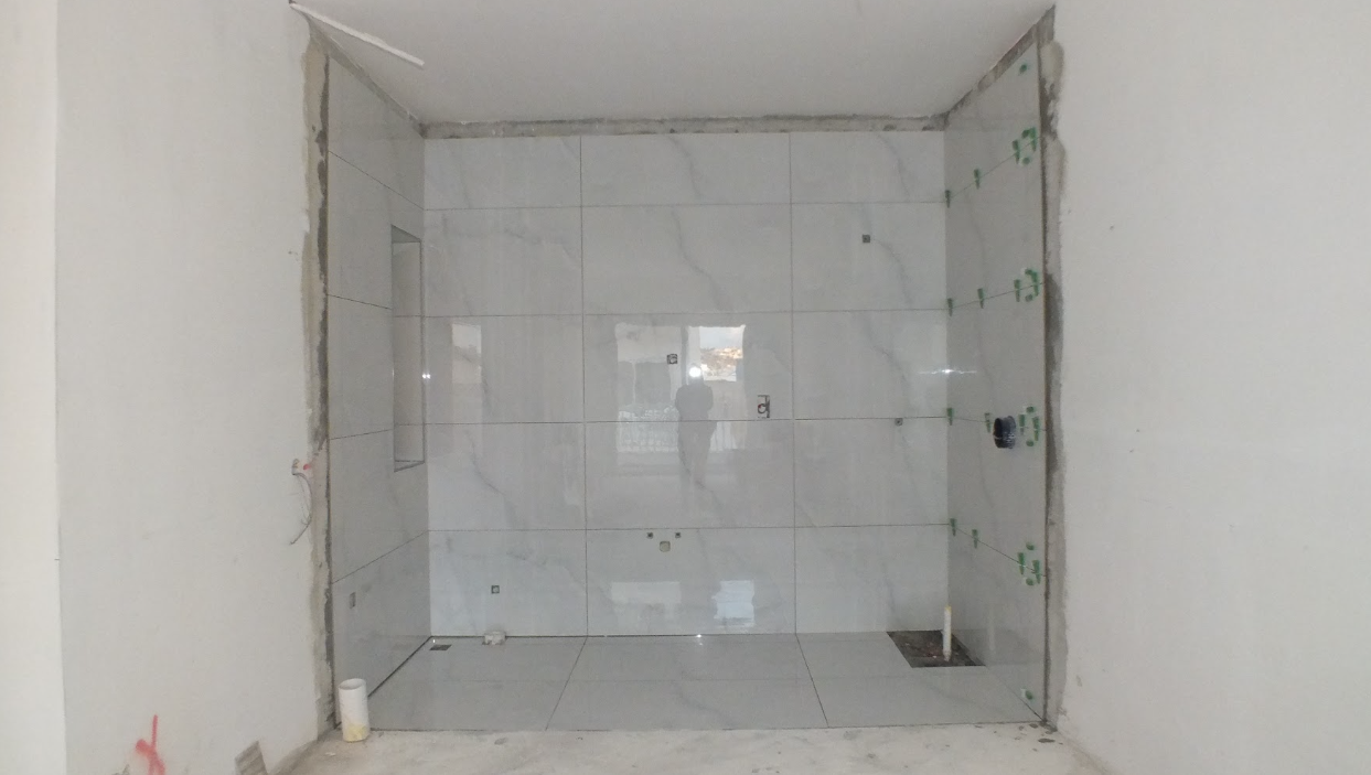 Bathroom under construction with white marble tiles on the wall, a small window, and plumbing fixtures installed.