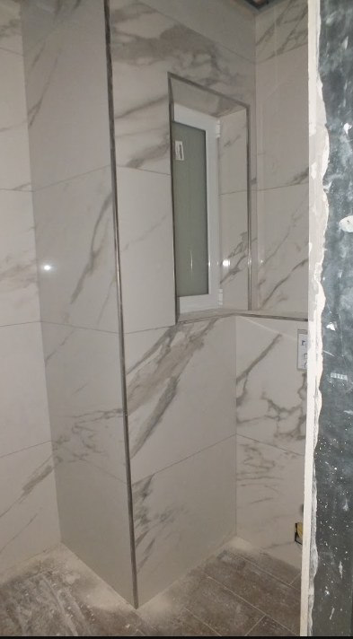 Marble tile bathroom wall with a small window and a partially finished built-in feature.