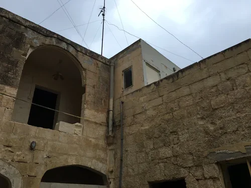 View of old stone buildings with concrete structure and wires against cloudy sky