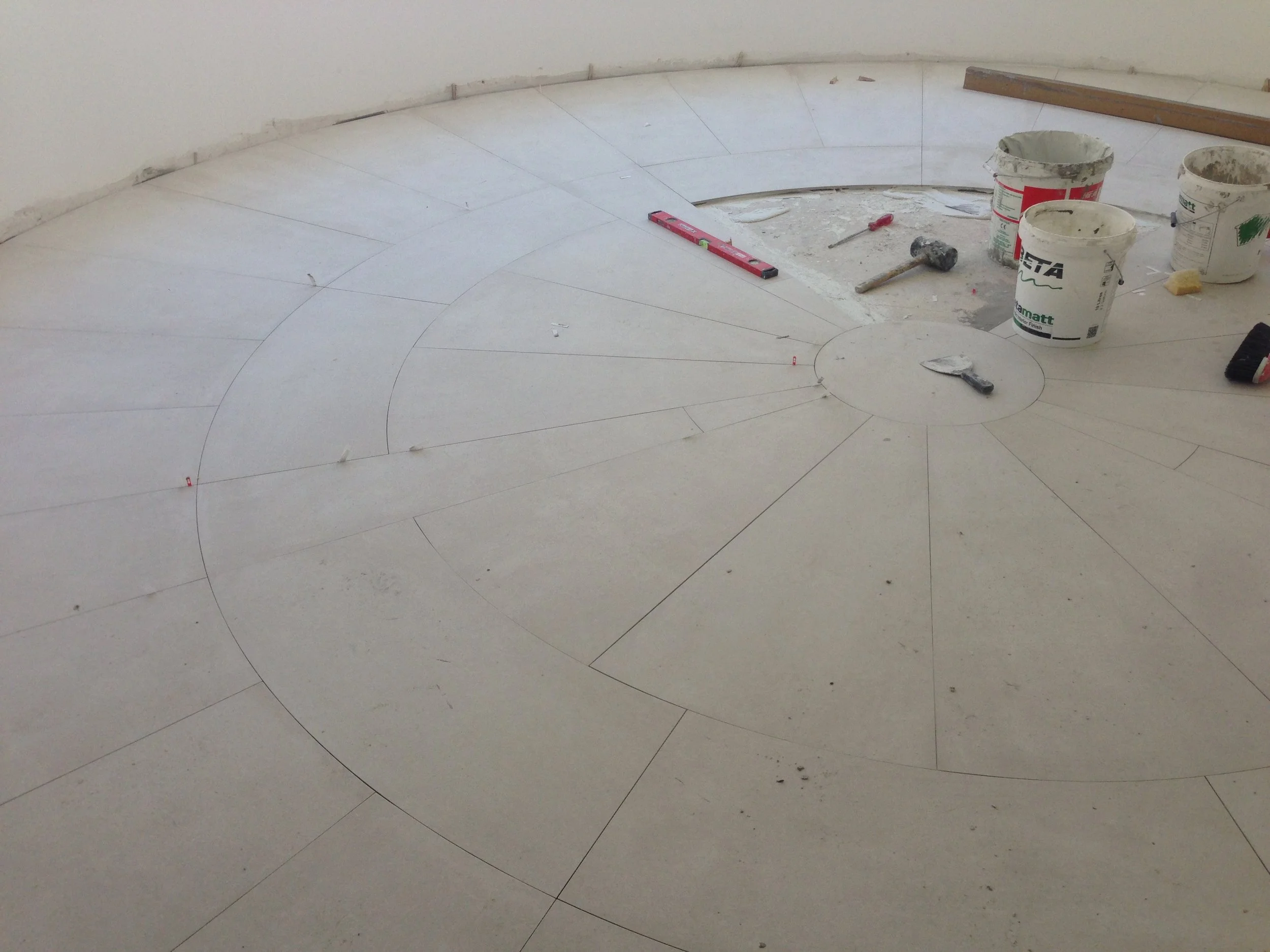 Interior of a room under construction with tiled flooring, construction tools and supplies such as buckets, a hammer, and level tools scattered on the floor.