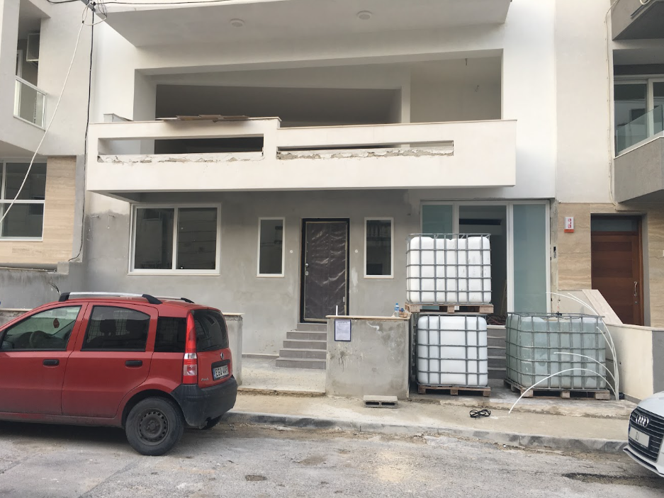 Construction site of a modern multi-story building with unfinished facade, construction tanks, and a parked red car in front.