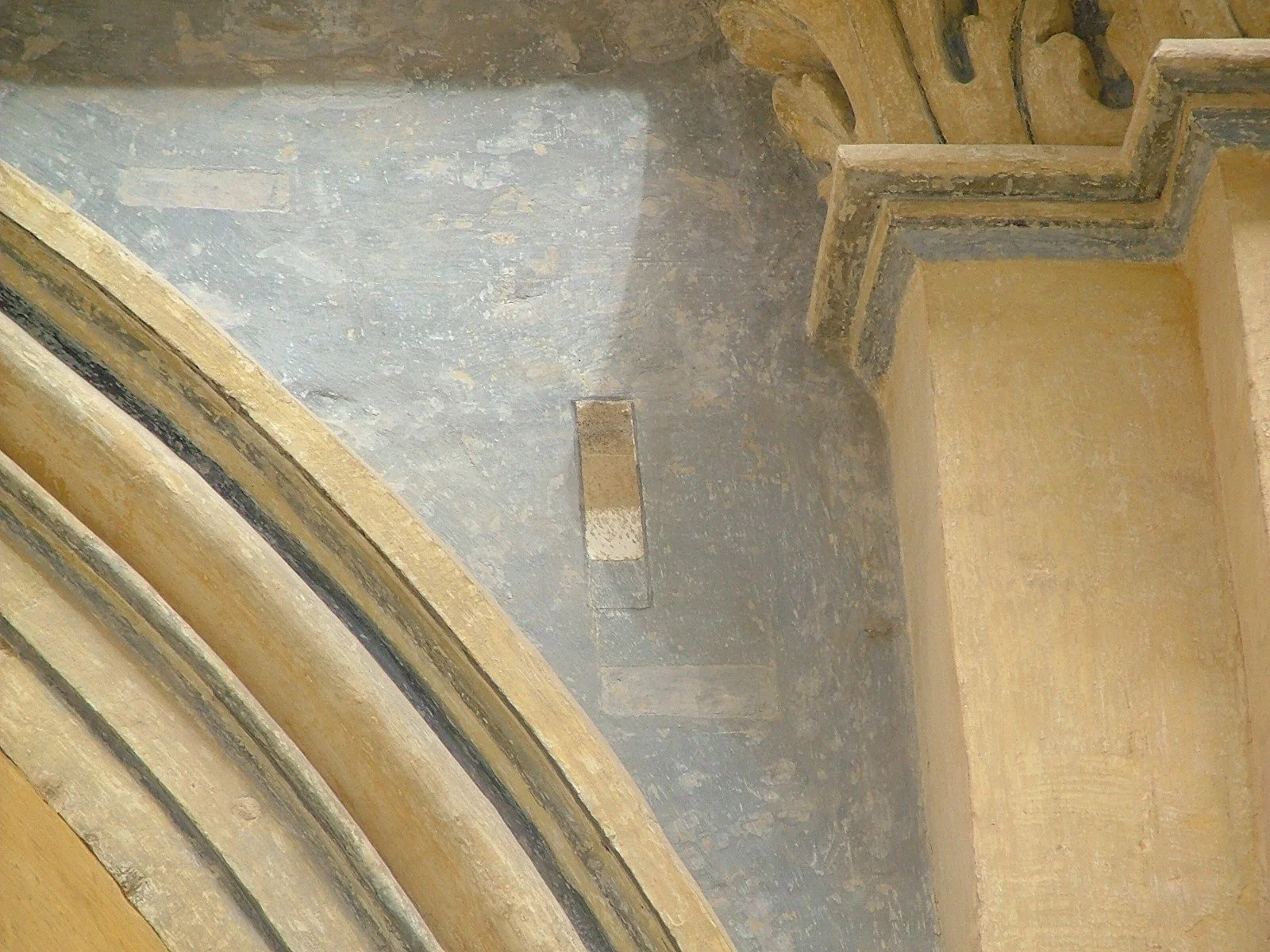 Interior view of a historic or religious building's ceiling and archway, showing aged plaster, ornate decorative molding, and a stone or concrete structure with visible wear and weathering.