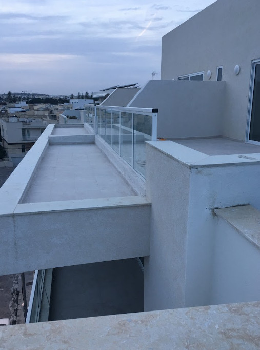 View of a rooftop balcony with glass railing and surrounding cityscape in the distance.