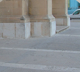 Close-up of a stone building corner with a sidewalk and a street curb.