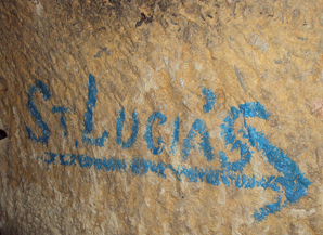Blue graffiti on a textured beige wall spelling 'St. Lucias' with an arrow pointing to the right.