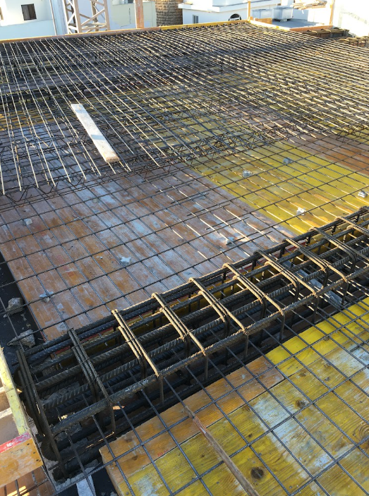 Construction site showing metal rebar and support framework laid out on a building roof for a concrete slab.