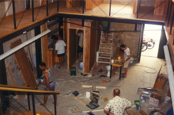 People working inside a building under construction, with tools and materials scattered around.