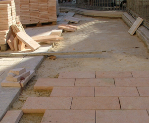 Construction site with pink paving stones, sand, and wooden planks, possibly for outdoor paving or landscaping.
