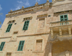 Close-up of a historic stone building with green window shutters and ornate architectural details