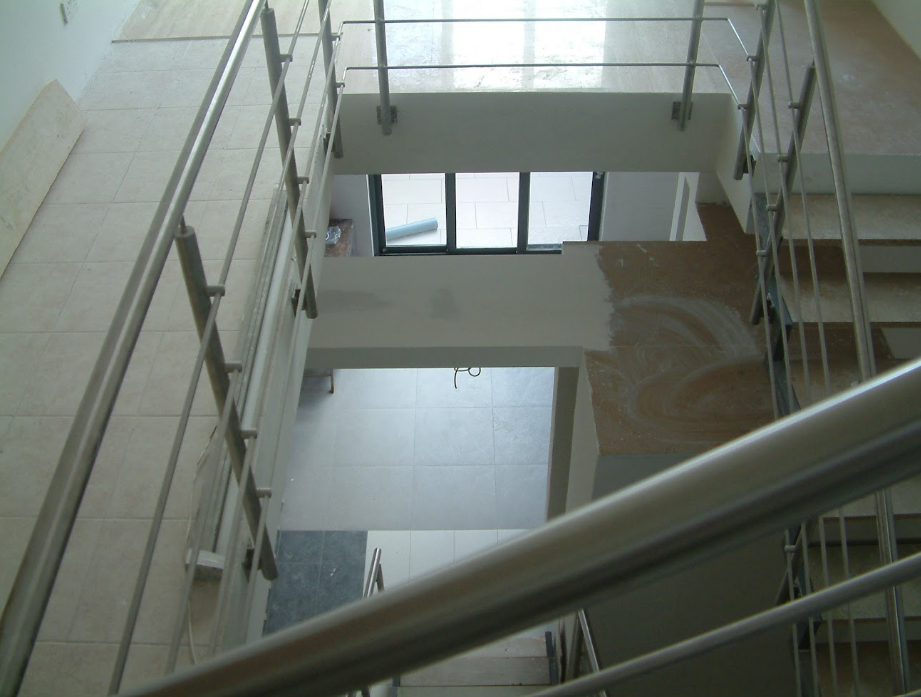 Interior of a building under construction with multiple floors, metal railings, stairs, and tiled floors, viewed from an upper level.