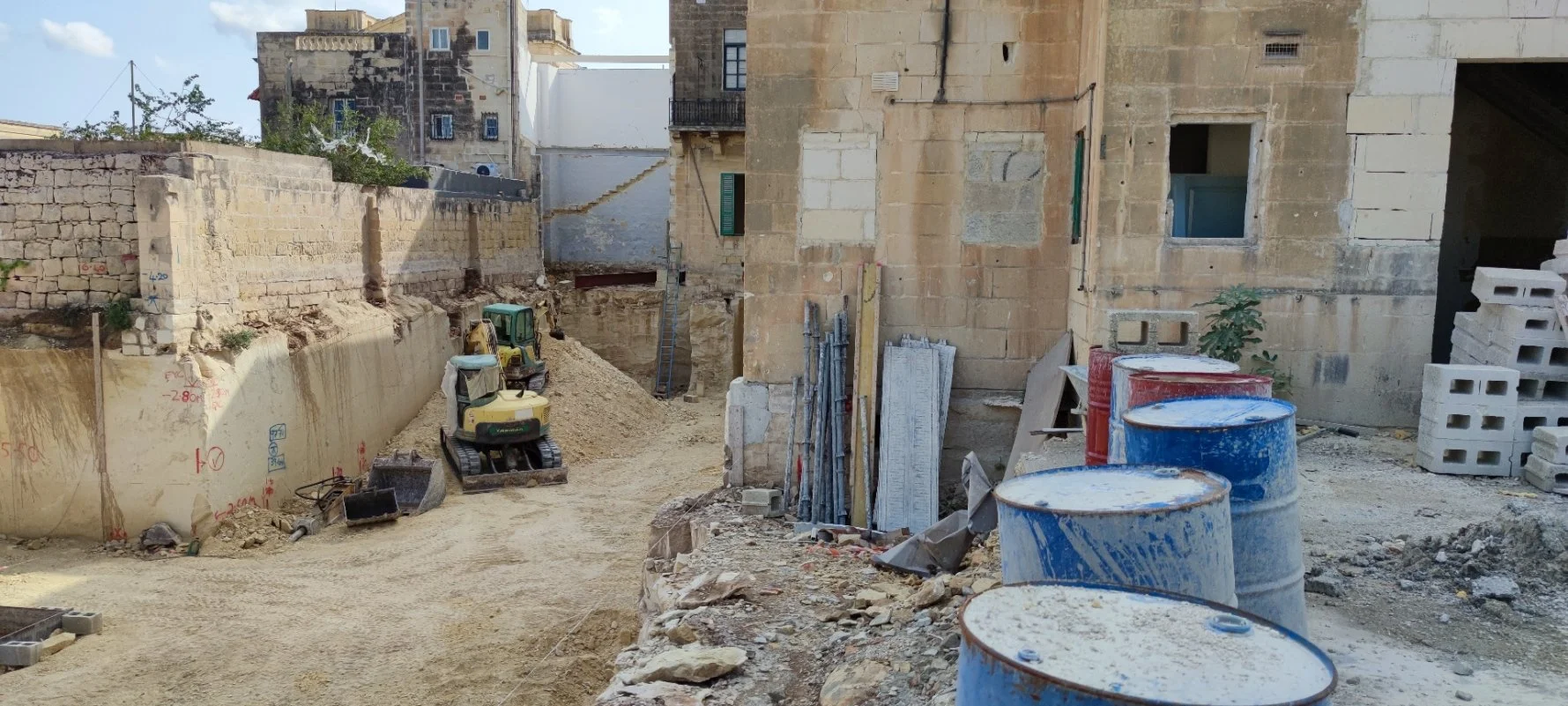 Construction site with dirt path, scaffolding, barrels, and partially built buildings.