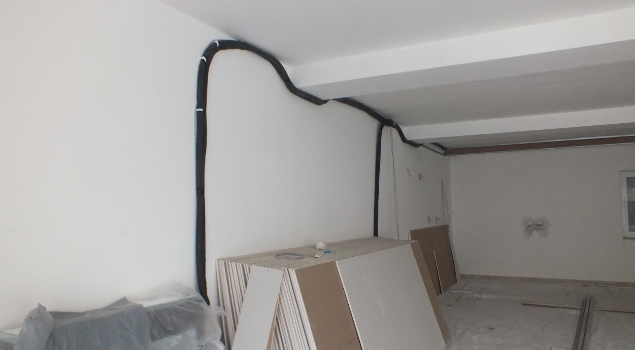 Room under renovation with electrical conduit running along the wall and construction materials leaning against the wall.