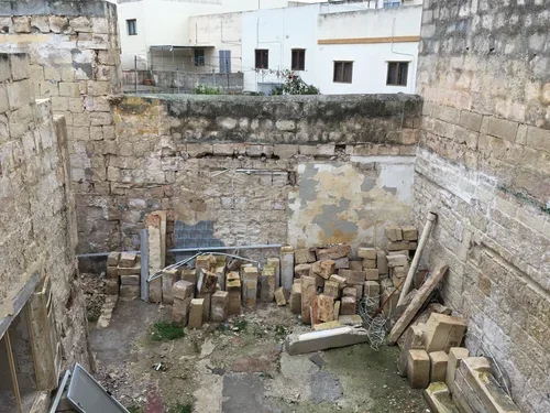 Scene of a construction site or backyard with bricks, wooden planks, and construction materials amid stone and brick walls.