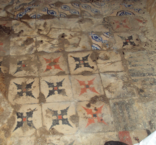 Old, weathered tiled floor with a pattern of black, red, and beige tiles, some showing signs of wear and damage.