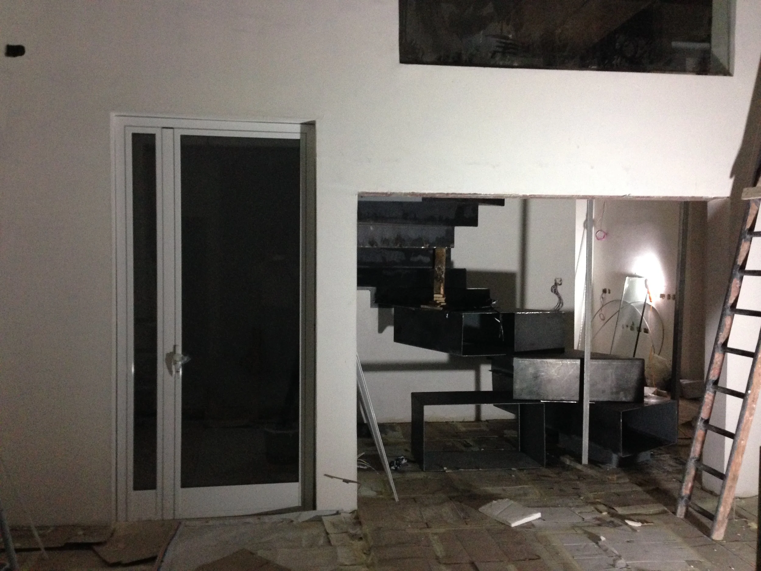 Room under construction with a ladder, black shelving unit, and partially finished walls at night
