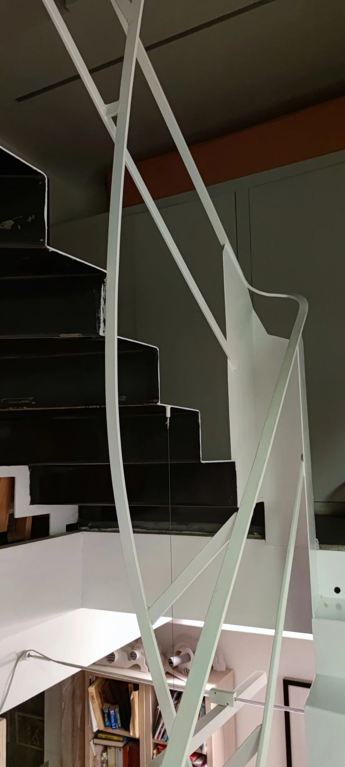 Indoor staircase with white metal railing, black steps, and green walls. Bookshelf visible in the background.