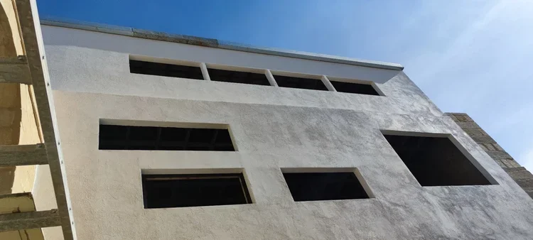 Photo of a white building under construction with several rectangular windows and a clear blue sky in the background.