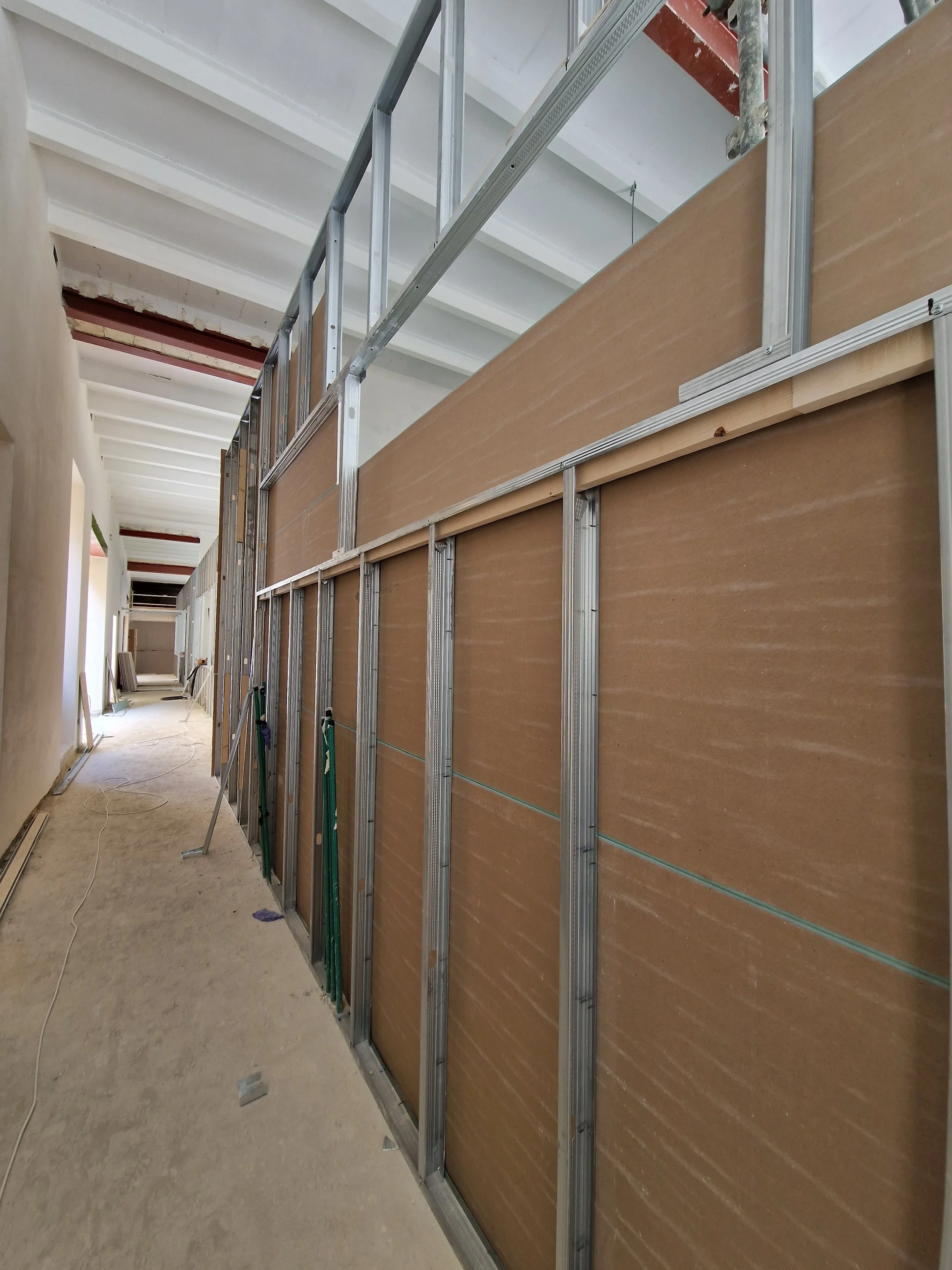 Interior view of a building under construction with metal framing and drywall panels installed on the walls, and an unfinished ceiling.