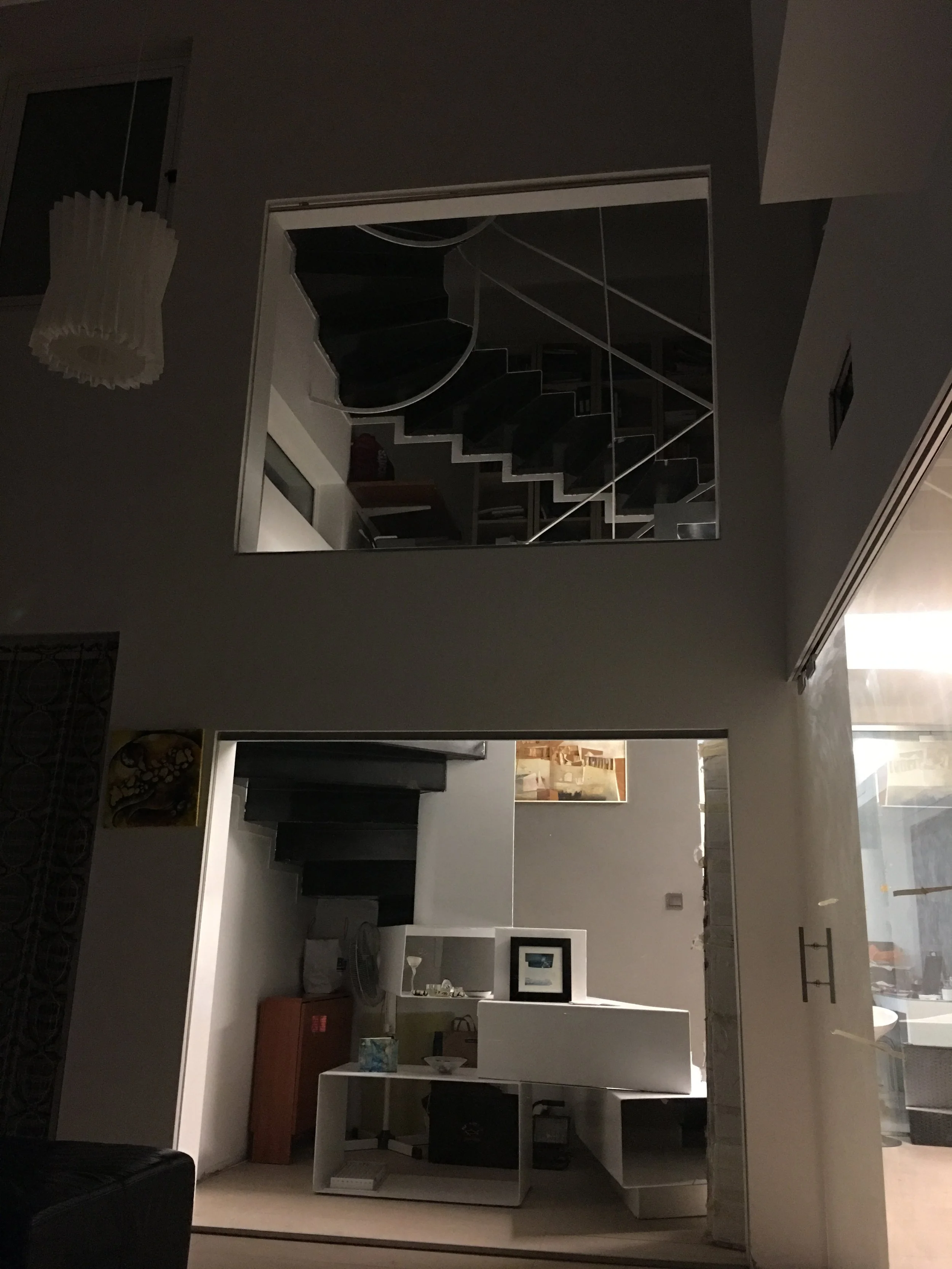 Living room with staircase reflected in mirror, various furniture items, wall art, and a hanging light fixture.