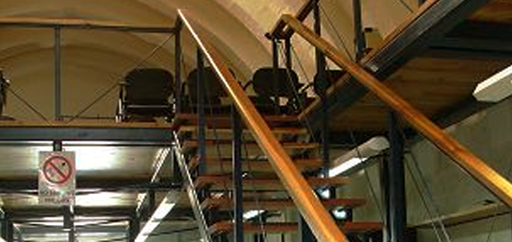 Indoor space with metal and wooden stairs, black chairs in the background, and a no-smoking sign on the wall.