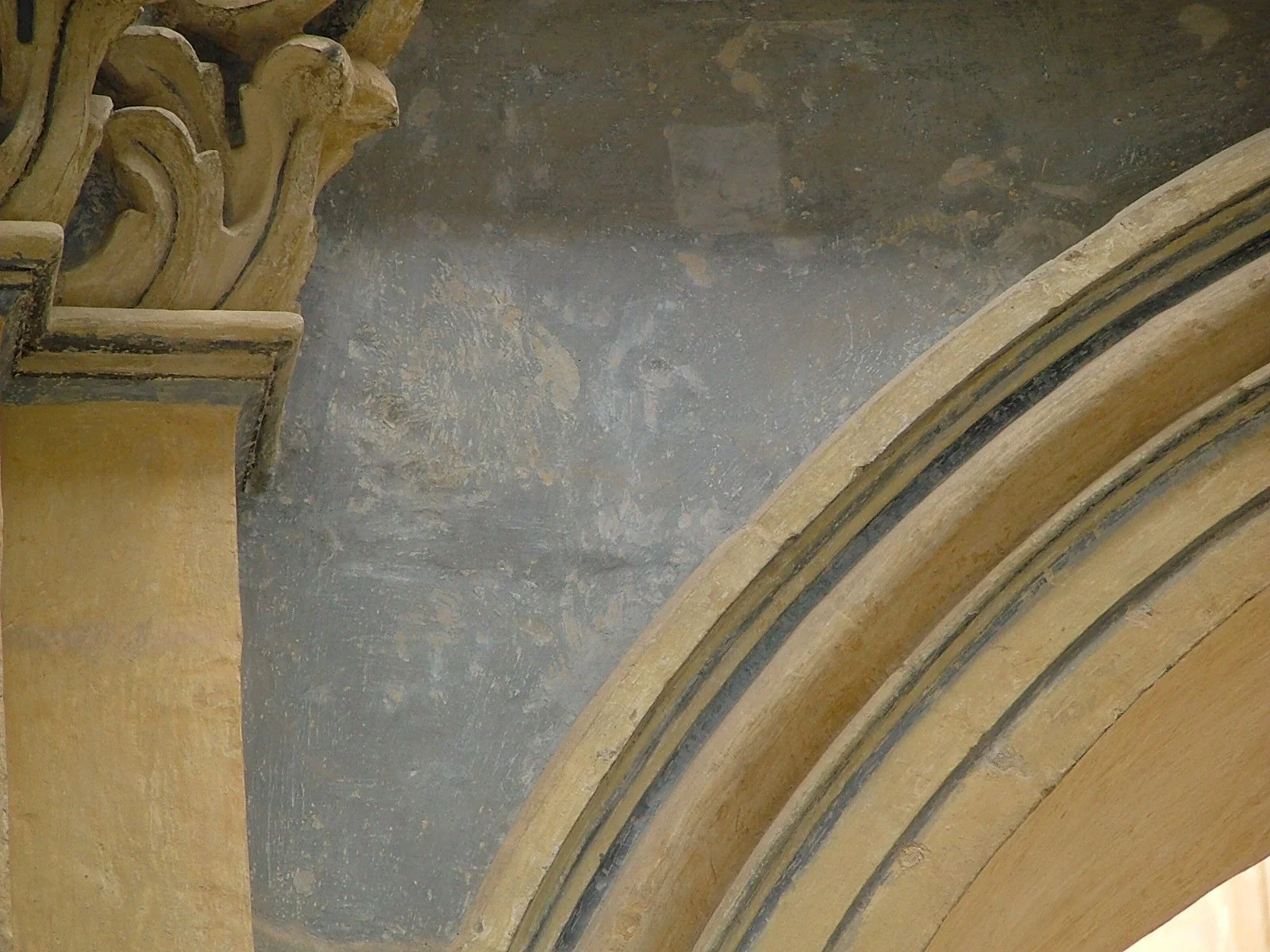 Close-up of a section of ornate architectural detail, including curved molding and decorative element, with a portion of the ceiling visible, showcasing aged and textured surfaces.