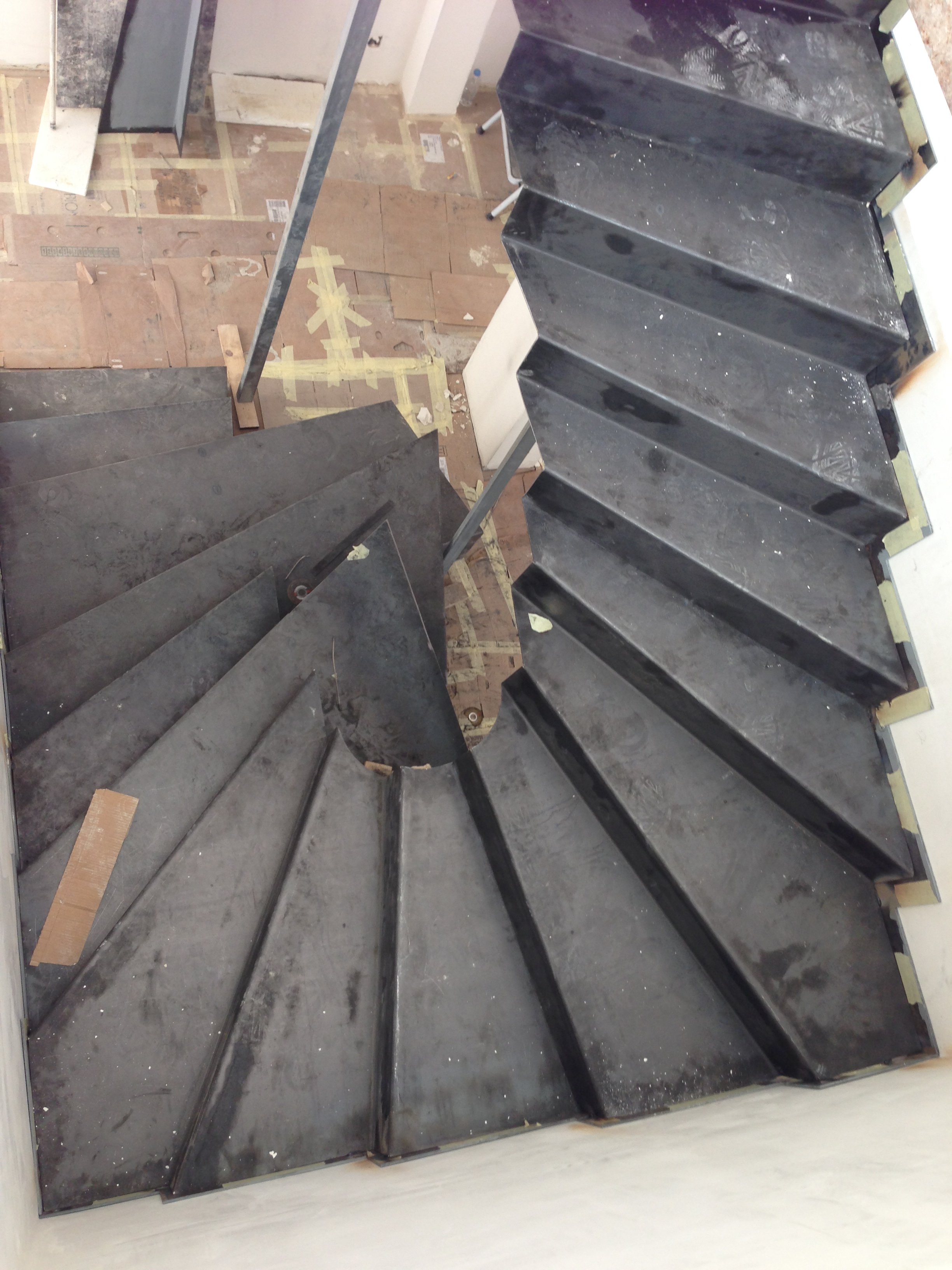 View from above of a black granite staircase with moderate dust and construction debris, with wooden flooring and tools visible in a construction or renovation site.