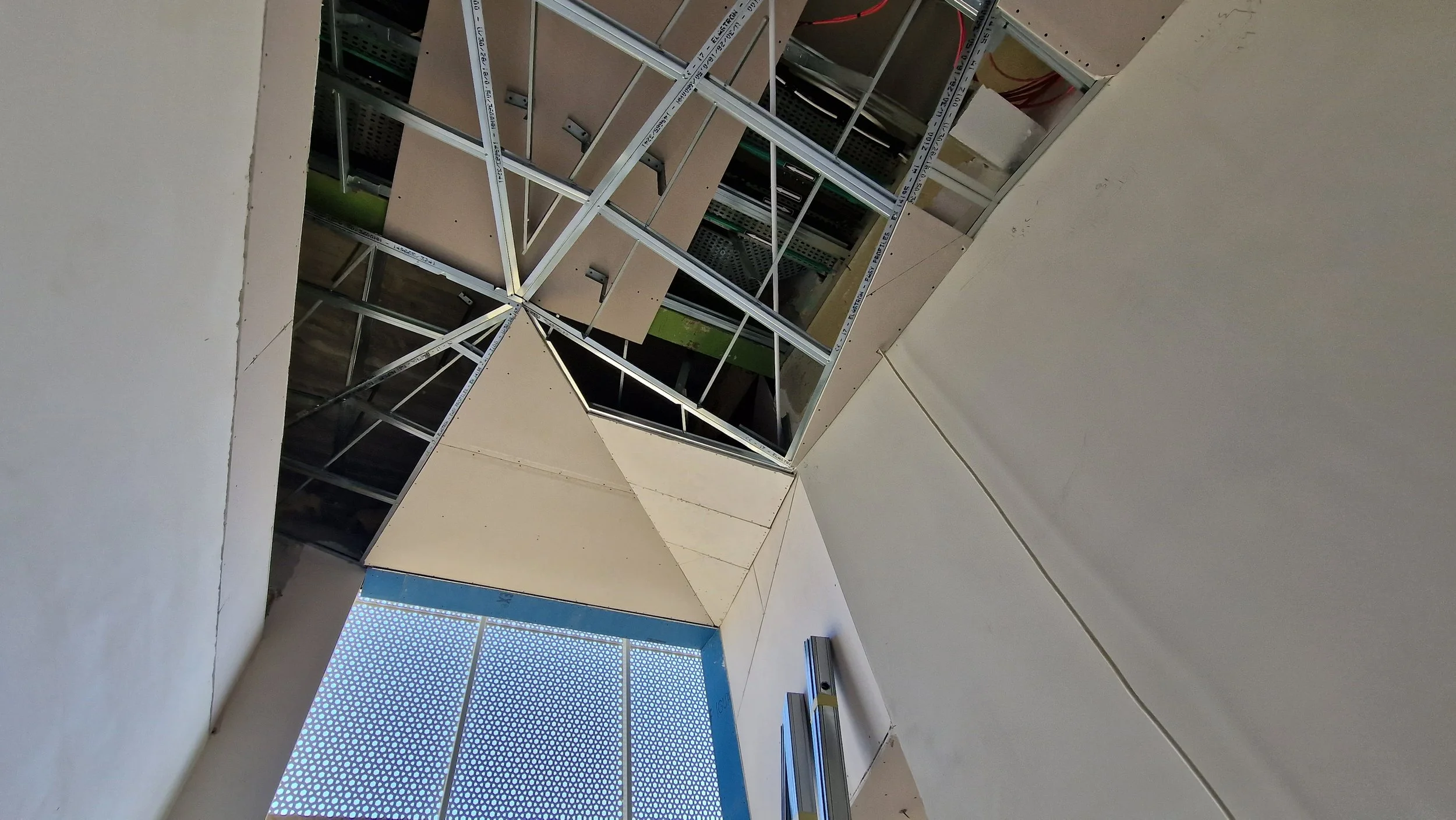 A ceiling under construction with metal framing and drywall panels, showing some wires and installation materials.