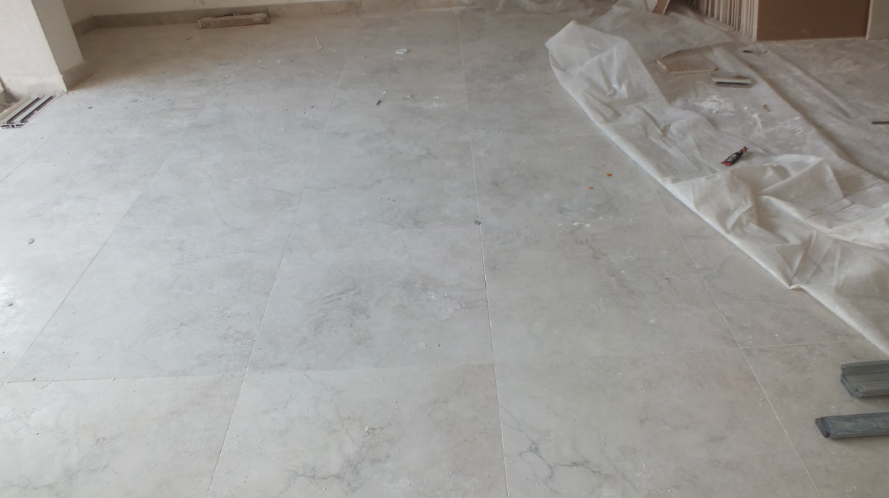 Incomplete tiled floor in a room under construction with construction tools and plastic sheeting.