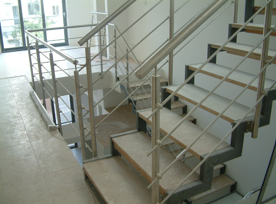 Interior view of a modern staircase with metal handrails and wooden steps in a building with large windows.