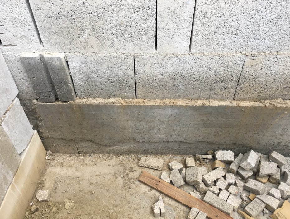 Construction site with cinder blocks stacked against a wall, some bricks and debris on the ground.