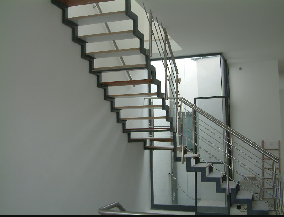 An unfinished modern staircase with metal frame and wooden steps, located inside a building near large glass windows.