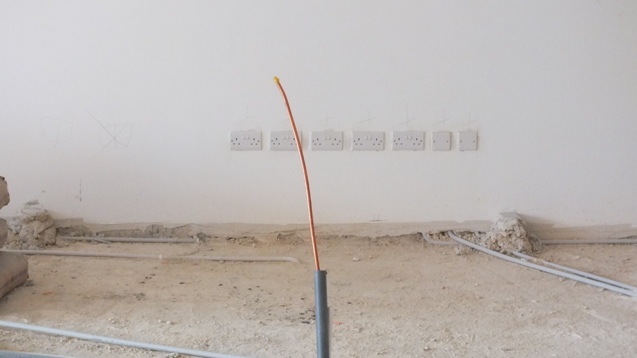 Construction site with unfinished flooring and electrical outlets on the wall.