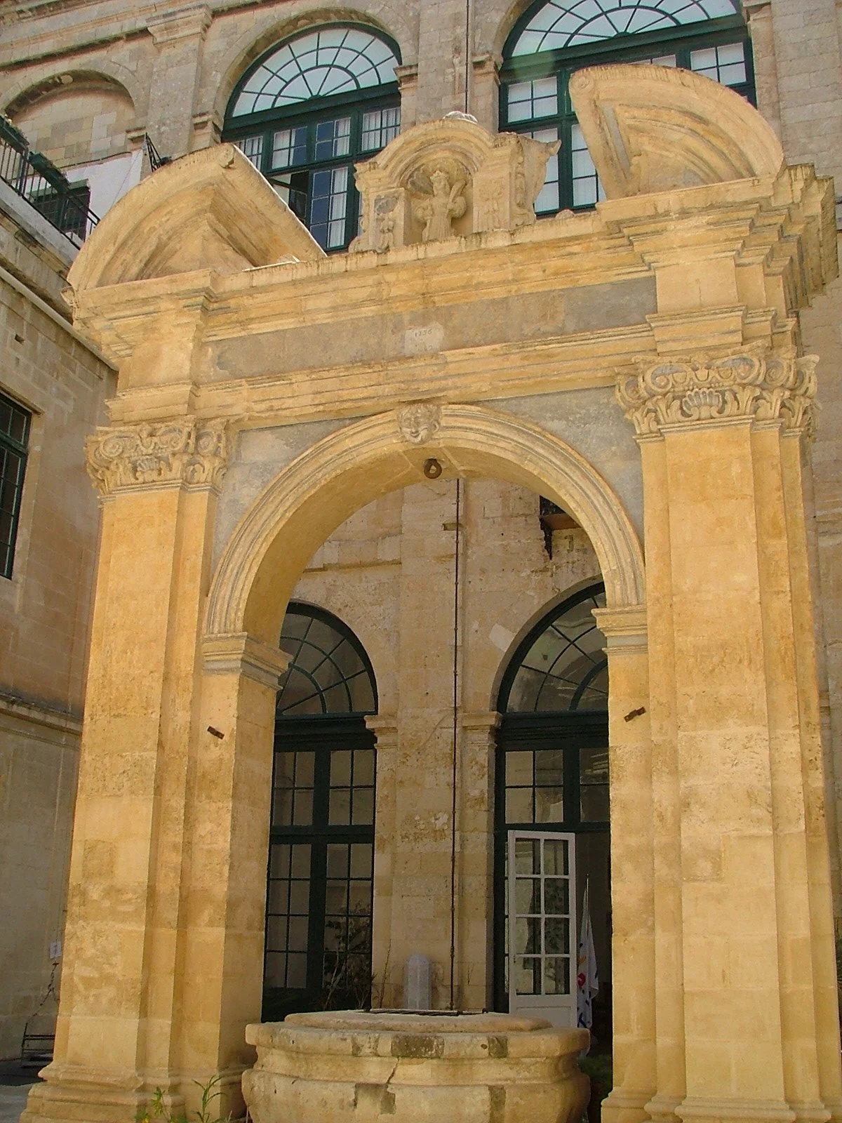 Ancient stone archway and fountain in a historic building courtyard, with large arched windows in the background.