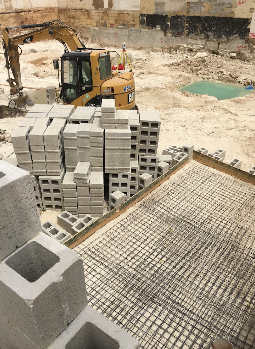 Construction site with concrete blocks, a small excavator, and a reinforced steel framework for a floor.