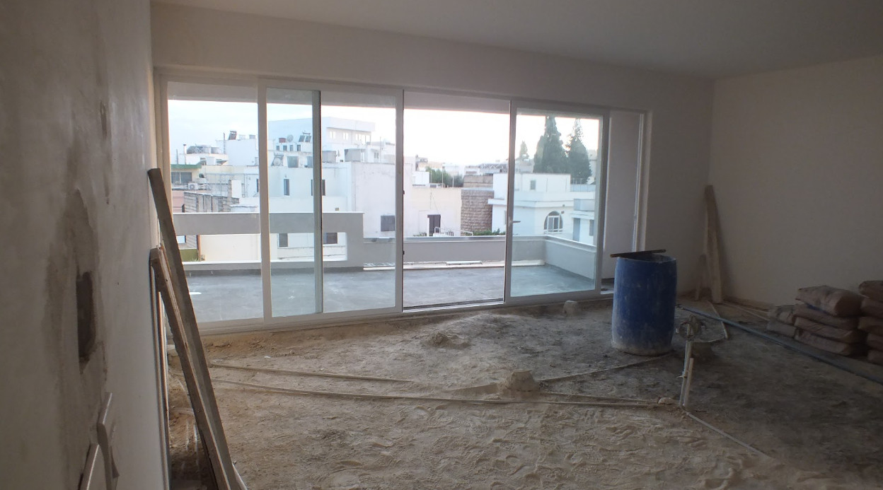 Room under construction with a large sliding glass door, construction materials, and tools, overlooking neighboring buildings